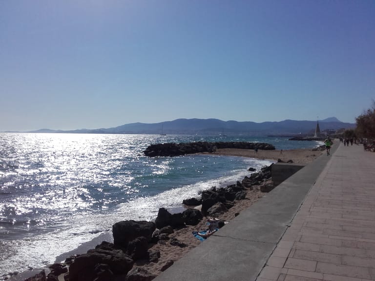The seafront promenade at Portixol in Palma, a paved walk running above a small rocky cove, with the bay and hills beyond.