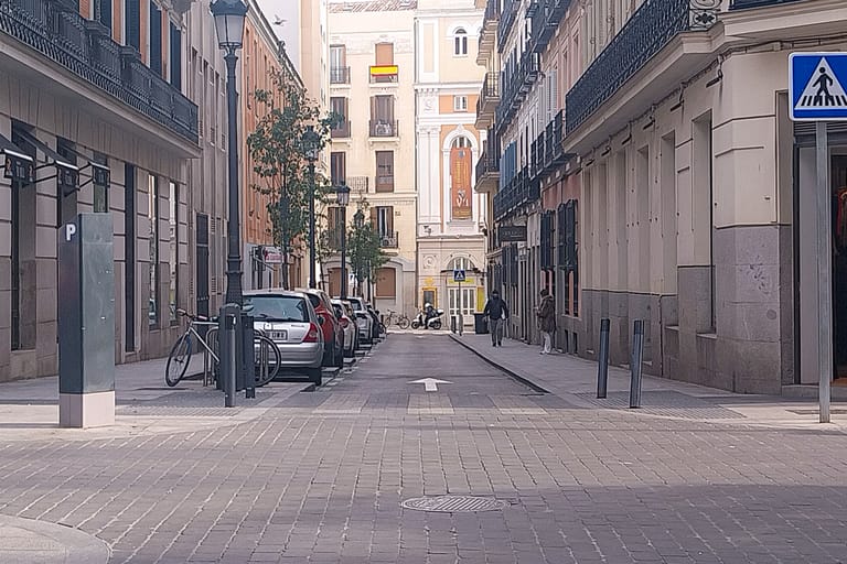 A quiet historic side street in central Madrid lined with balconied stone townhouses in soft daylight.