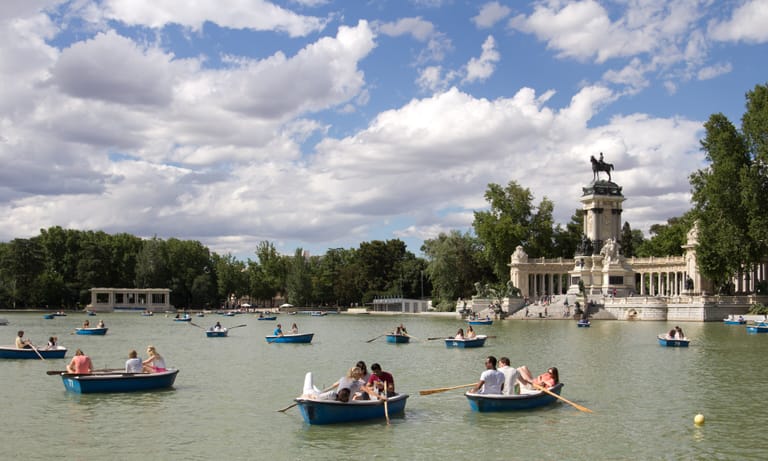 Rowing boats on the Estanque of Madrid's Retiro park, the colonnade of the Alfonso XII monument behind them under a bright sky.