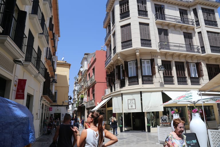 A lively pedestrian street in Málaga's historic centre with café terraces and ornate facades in warm Andalusian light.
