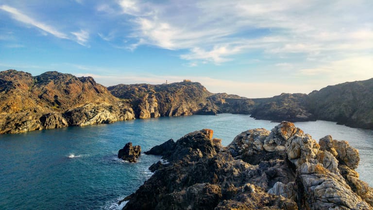 The rocky cove of Cala Culip at Cap de Creus, calm turquoise Mediterranean water meeting weathered coastal rock beneath a soft sky.