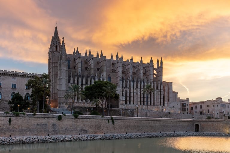 Palma's Gothic cathedral above the old sea wall at Parc de la Mar, under a warm evening sky.