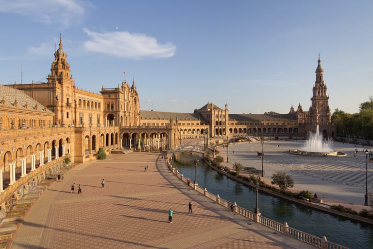 The brick and tiled crescent of Seville's Plaza de España, its canal and bridges in warm afternoon light.